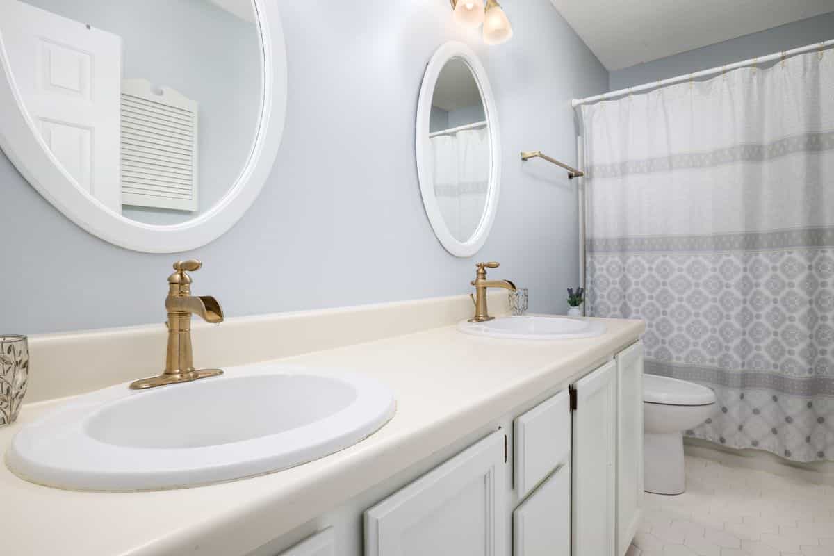 Bathroom vanity with gold faucets and round mirrors illustrating round mirror decor over a vanity Modern bathroom with dual sinks, gold faucets, and round mirrors, illustrating round mirror decor over a vanity