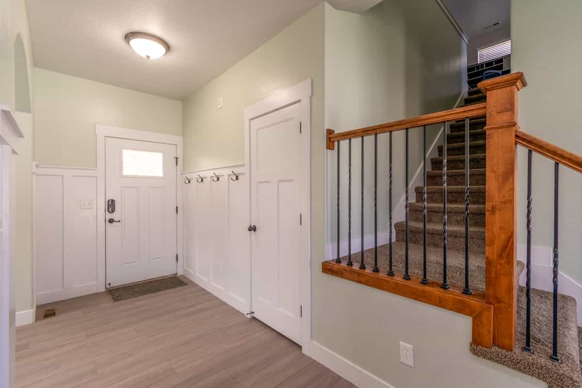Wall-mounted hooks beside an entry door illustrating mounting height for an entryway mirror with hooks Bright entryway with wall-mounted coat hooks beside a white door, showing how to mount an entryway mirror with hooks