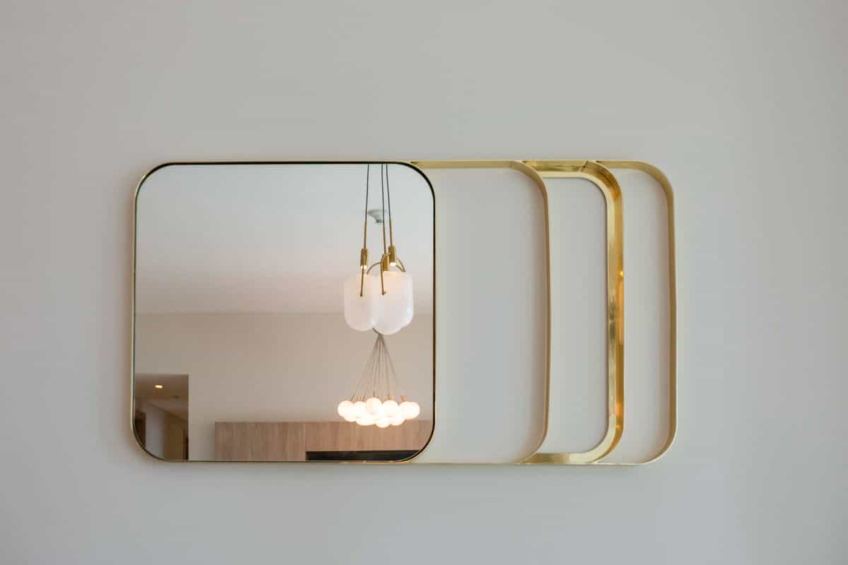 Wall mirror with a gold frame reflecting contemporary lighting, illustrating mirror frame and finish ideas