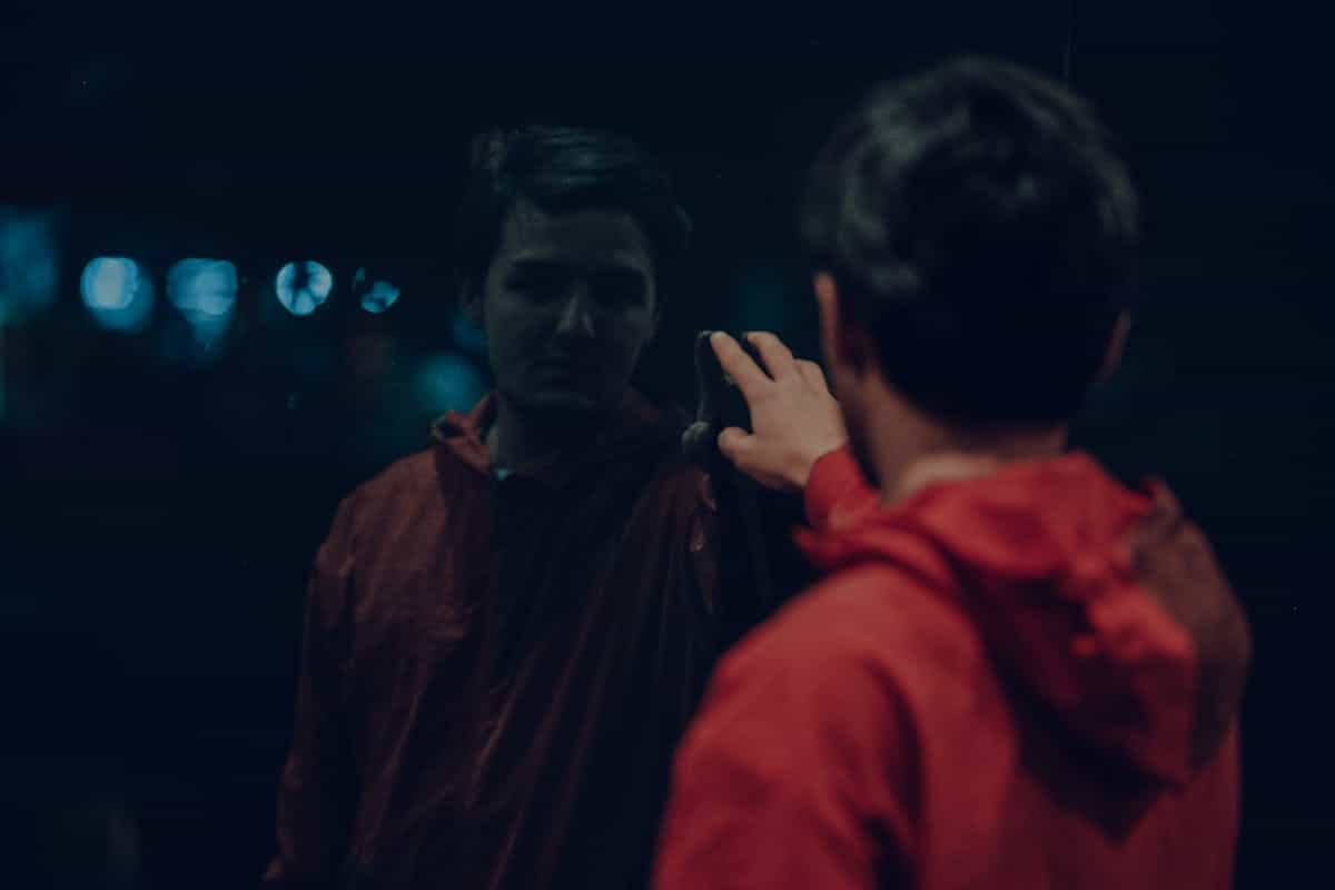 Person reaching toward dark reflective panel at night suggesting tactile curiosity across mirrored boundary