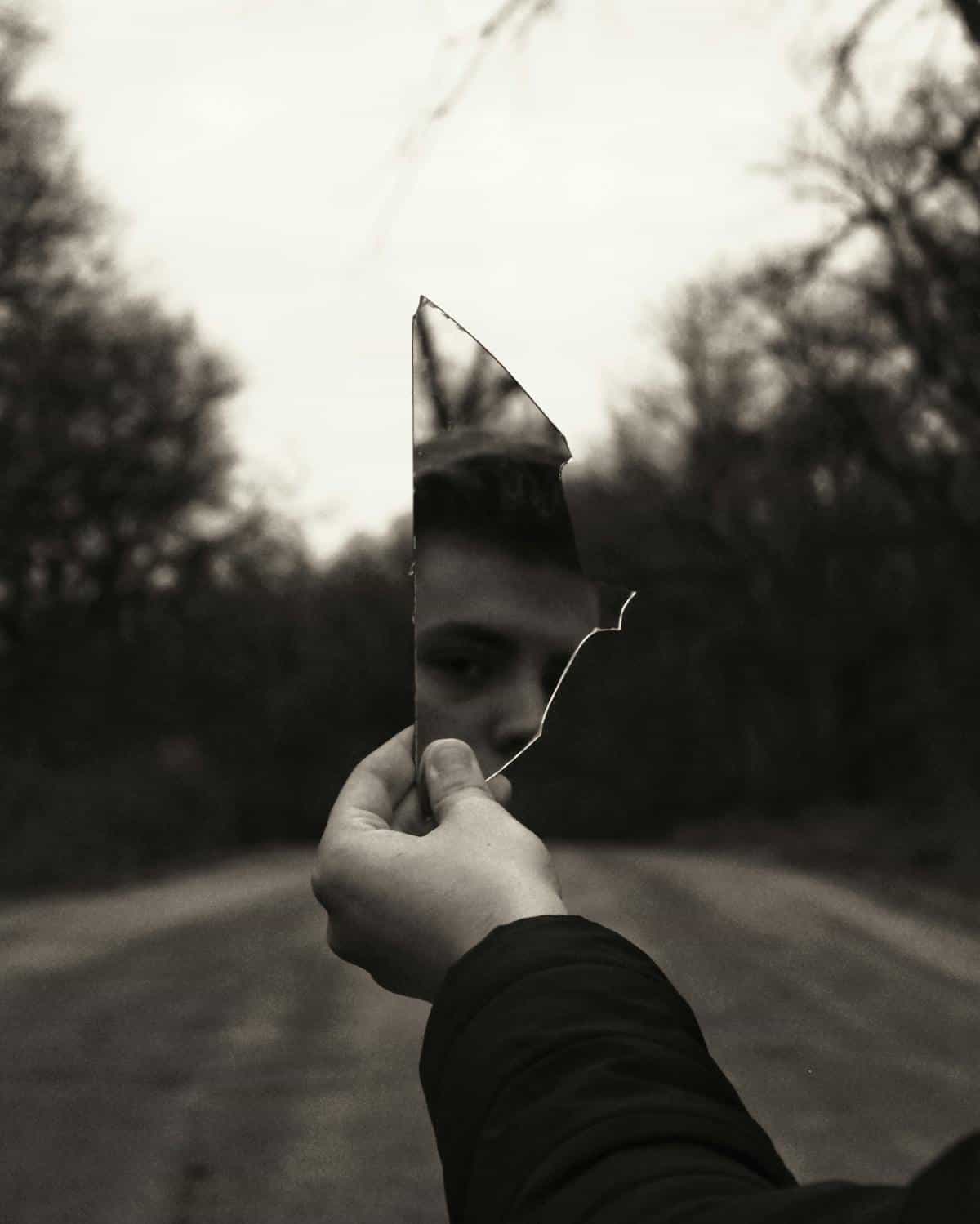 Grayscale photo of anonymous hands holding fractured mirror fragments toward diffused daylight