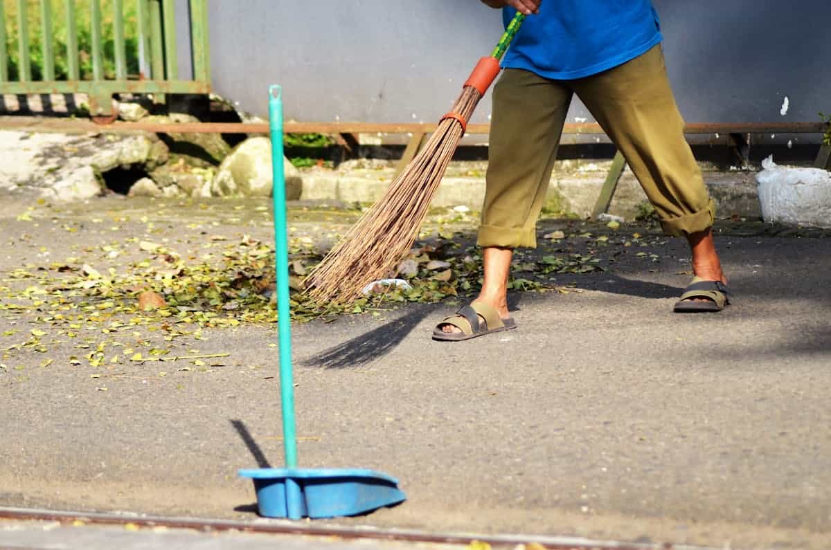 Person outdoors sweeping fallen leaves from a street with a broom suggesting thorough visible cleanup before finer methods