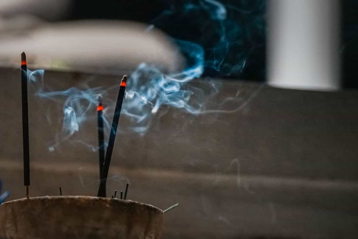 Close-up of burning incense sticks with rising blue smoke creating a calm and spiritual atmosphere representing cultural and spiritual cleansing practices across traditions