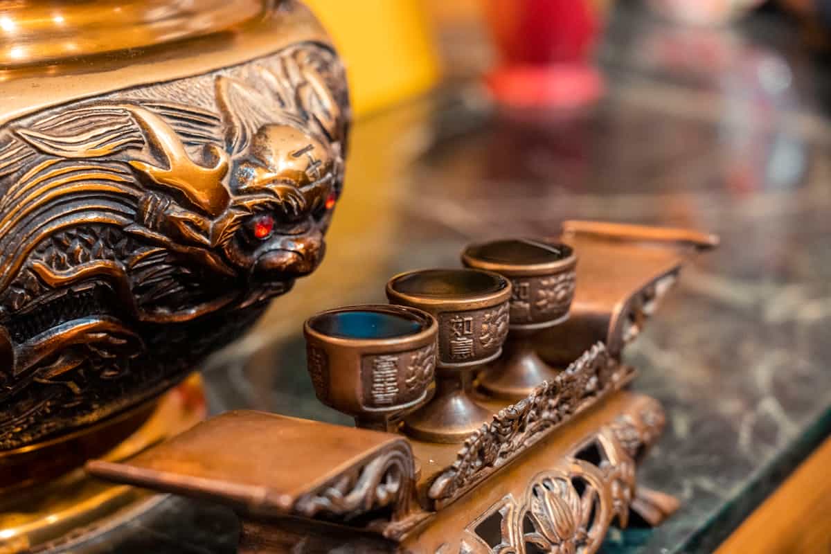 An ornate bronze religious figure alongside decorated chalices on a marble surface representing the sacred use of bronze in ancient worship and the connection between material objects and spiritual meaning in Scripture