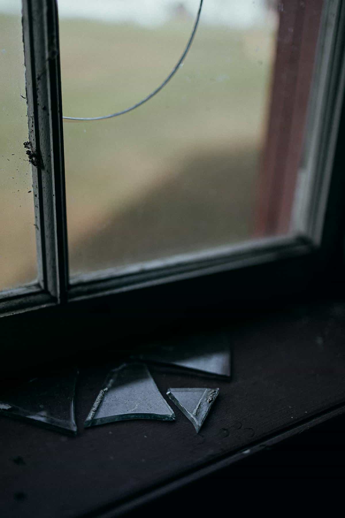 Broken window glass shards suggesting emotional rupture and warning themes in dreams Moody broken window glass with scattered shards on sill suggesting warning and emotional rupture in dreams