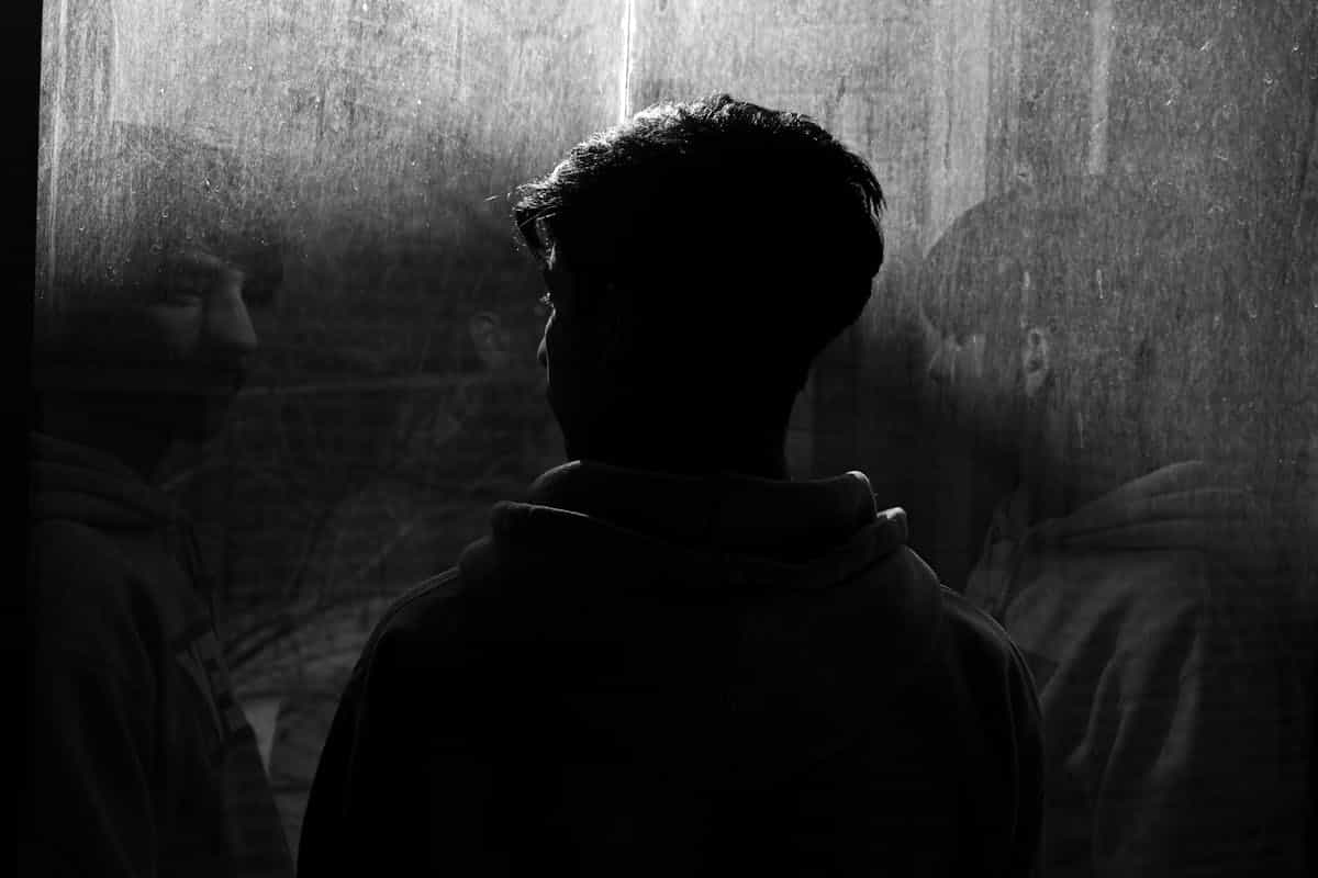 Silhouette of a man reflected on a window surface in a moody, contemplative scene evoking the shadow self and the hidden dimensions of the psyche explored through black mirror work