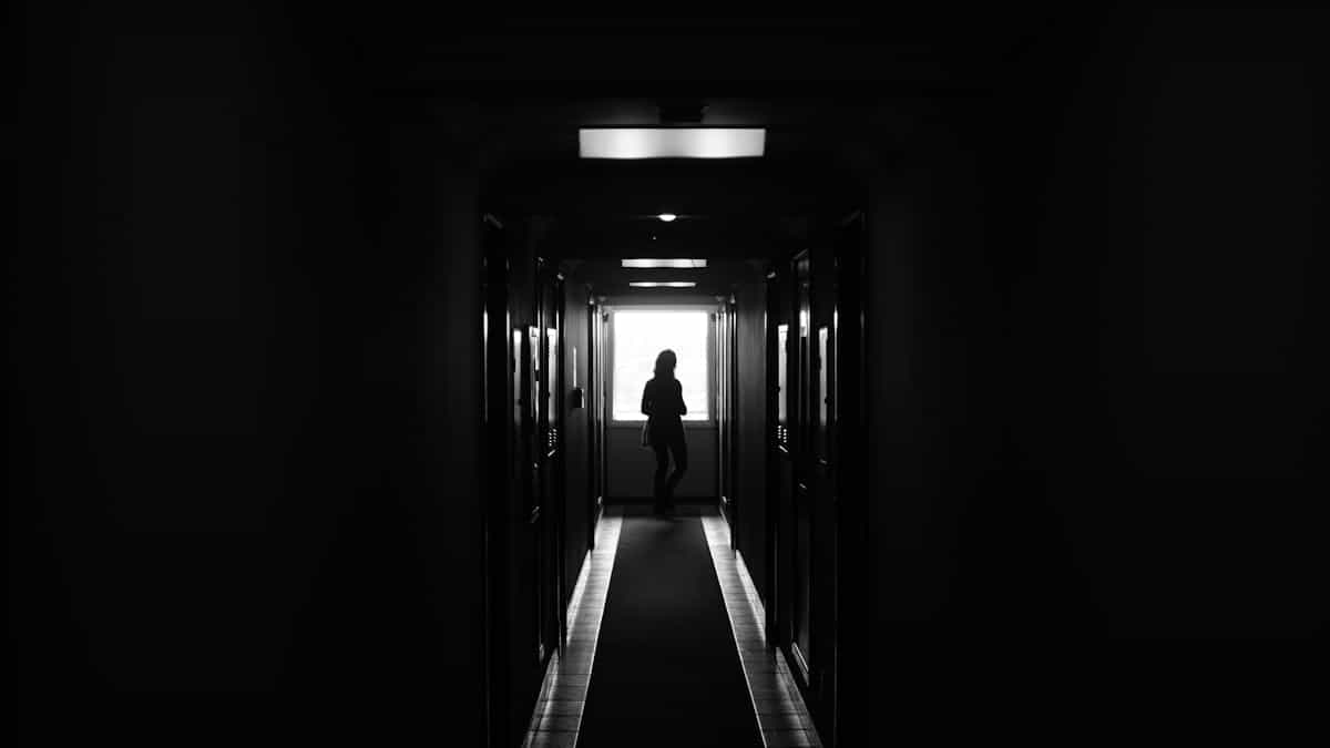 A dramatic silhouette of a lone figure standing in a dark hallway representing the threatening or distorted presence that can appear in mirror dreams