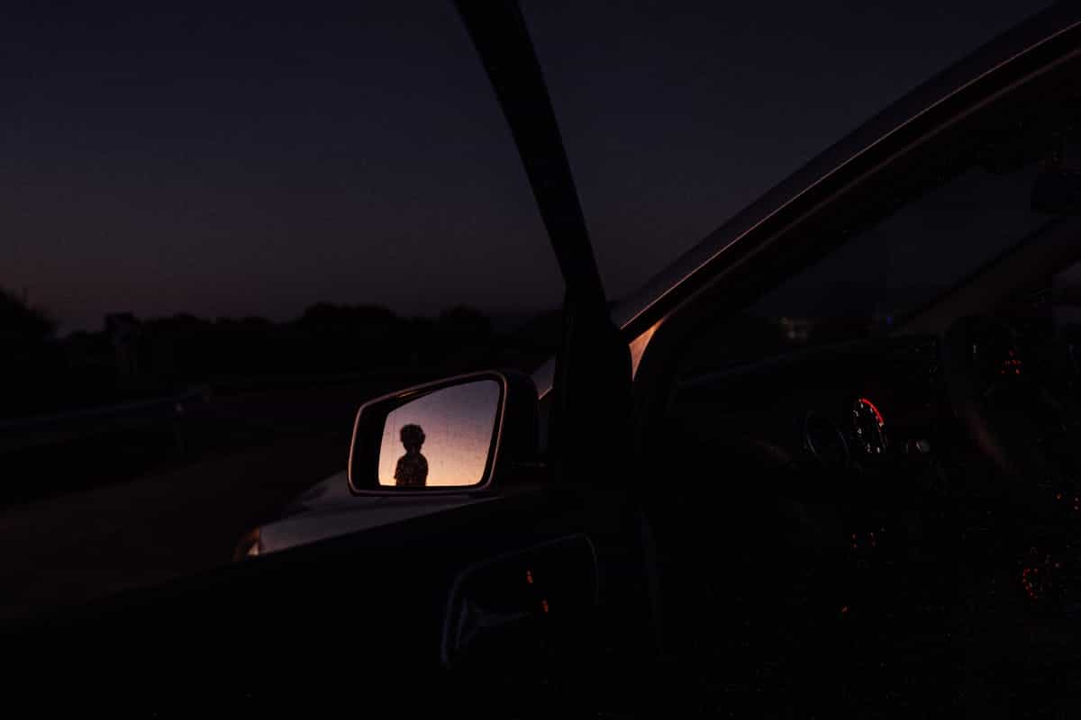 Nighttime urban glow reflected in vehicle side mirror illustrating liminal mirror symbolism between darkness and doubled city lights