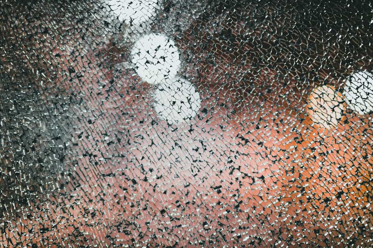 Photograph of shattered mirror glass pieces catching soft indoor light on a wooden surface