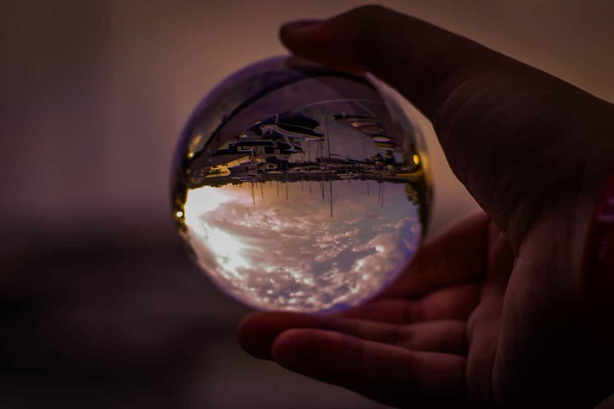 Hand holding a clear glass sphere reflecting a sunset harbor scene