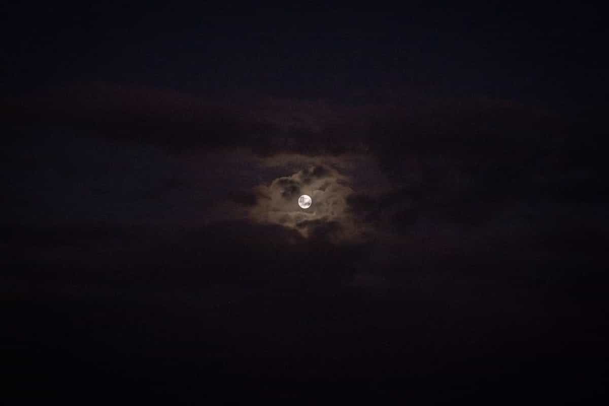 Mysterious full moon peeking through dramatic dark clouds in a serene night sky, evoking the lunar and absorptive spiritual energy harnessed in black mirror protection rituals