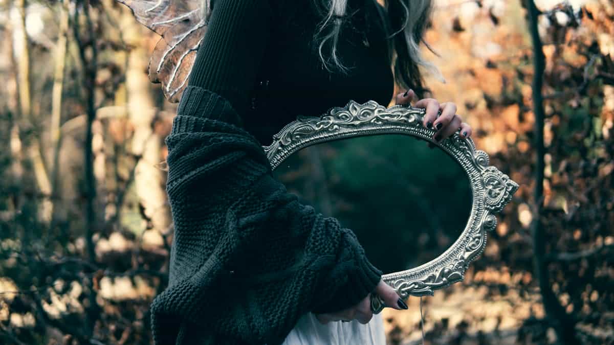 A woman holding an ornate mirror surrounded by autumn trees, representing global mirror folklore traditions