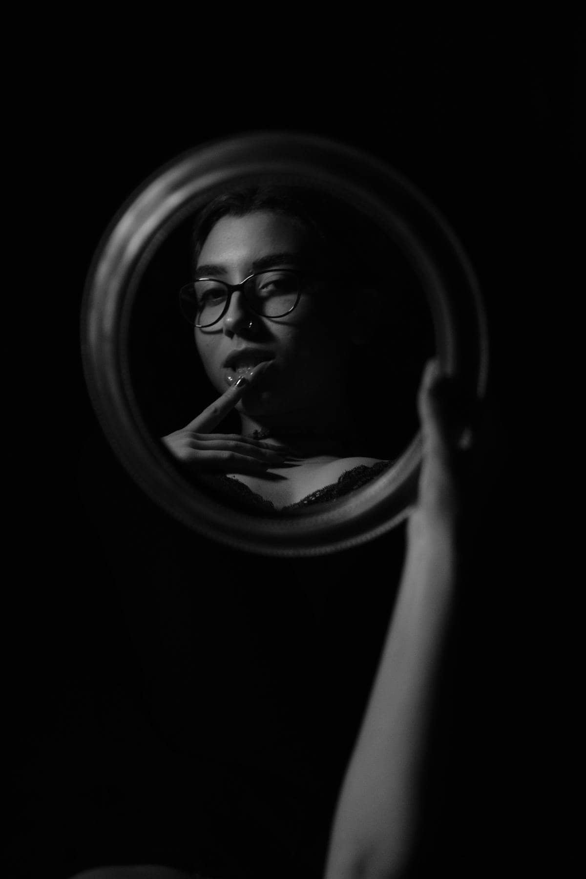Monochrome reflective portrait with eyeglasses and handheld mirror emphasizing contrast between silhouette and mirrored detail