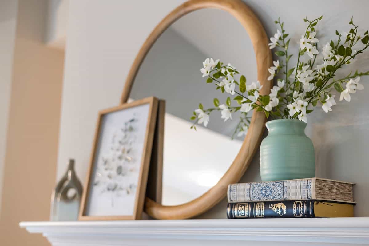 Framed decorative mirror styled with flowers and books illustrating round mirror frame styles Stylish interior with a framed mirror, vase of flowers, and books on a shelf, illustrating round mirror frame styles