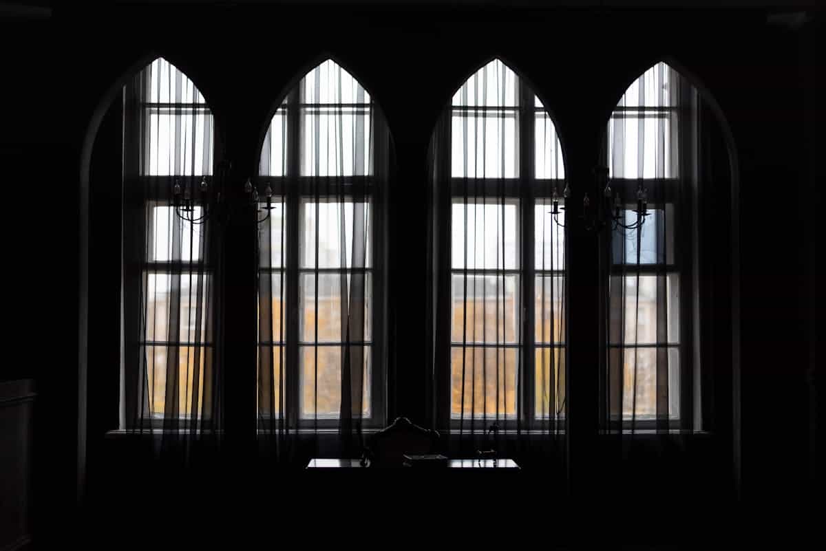 Dramatic silhouette of tall Gothic windows framed by curtains in low light