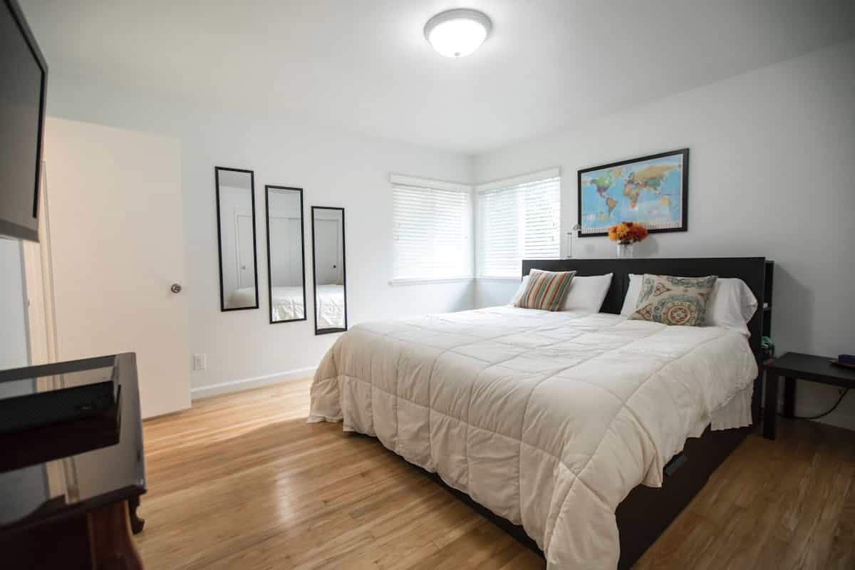 Bright bedroom with wood floors, a large bed, and mirrors, illustrating a full-length wood mirror