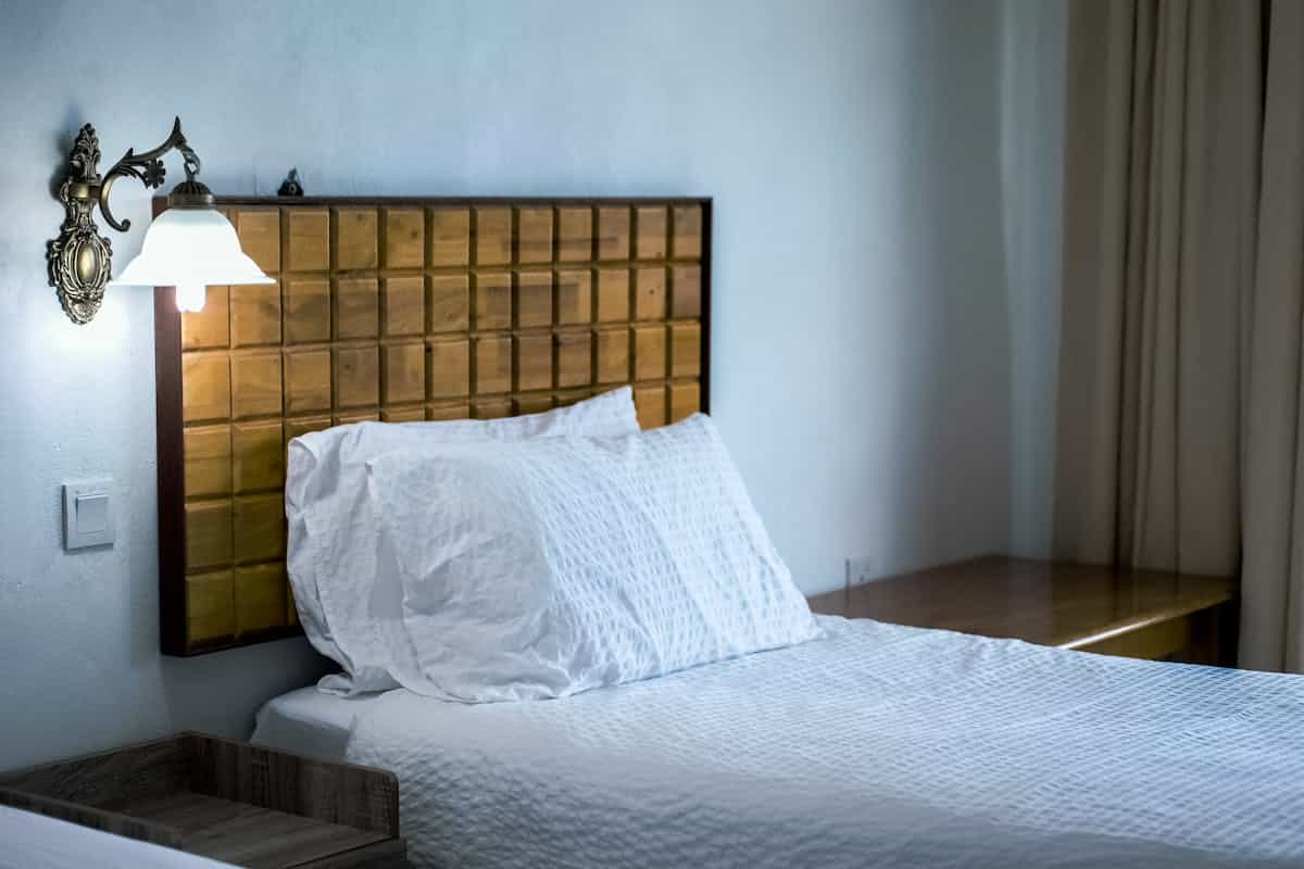 Bedroom with a solid wooden headboard against the wall and a wall lamp, illustrating feng shui headboard rules
