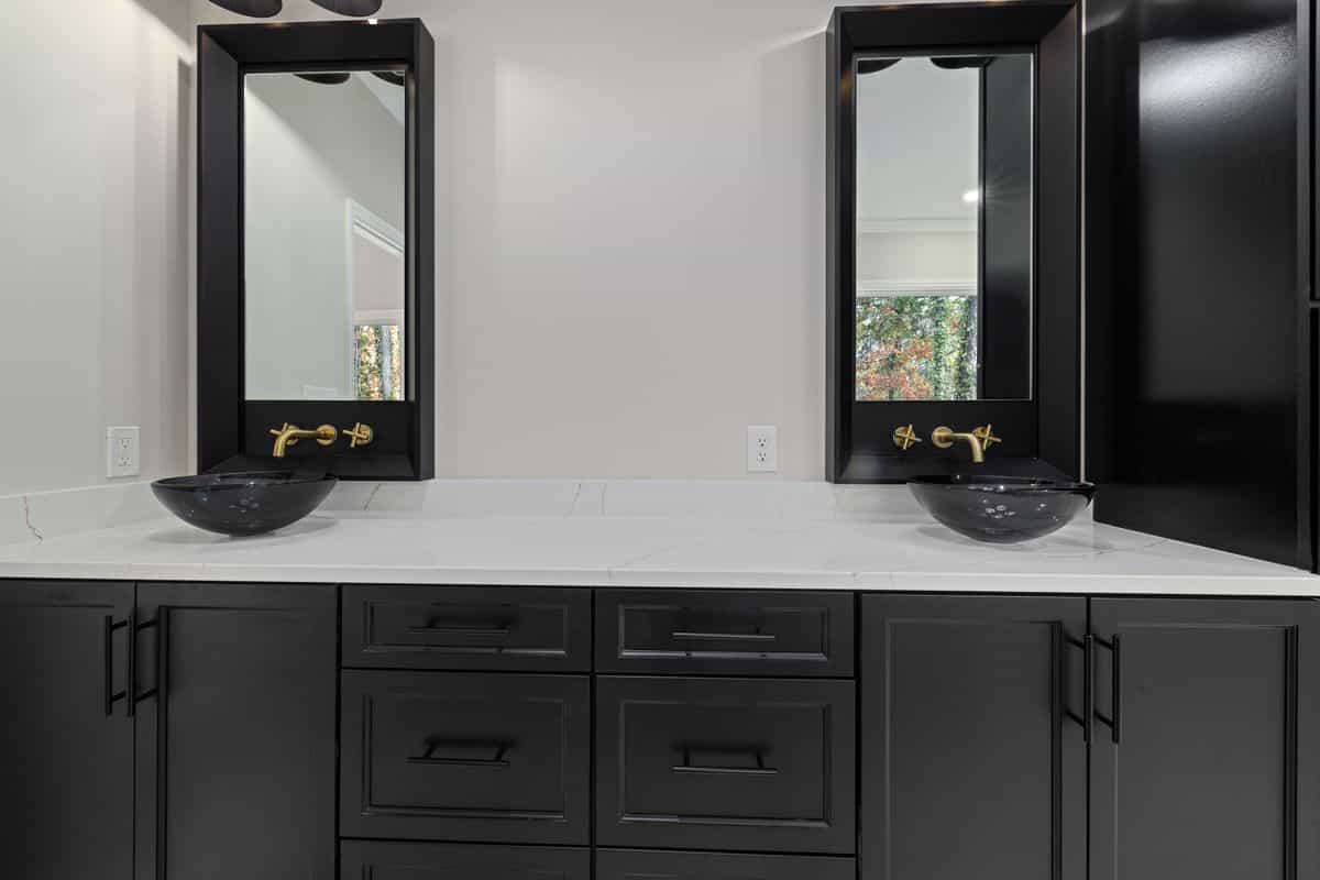 Black cabinets with gold hardware illustrating how to pair black mirror decor with warm metallics Bathroom with black cabinets, vessel sinks, and gold hardware, illustrating black mirror decor paired with metallics