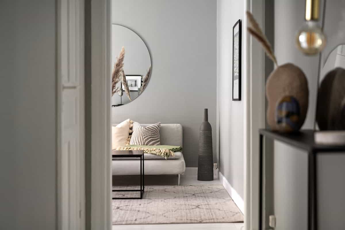 Living room with a round mirror above a sofa illustrating round mirror placement over furniture Cozy living room with a sofa, round mirror, and elegant furnishings, illustrating round mirror placement over a sofa