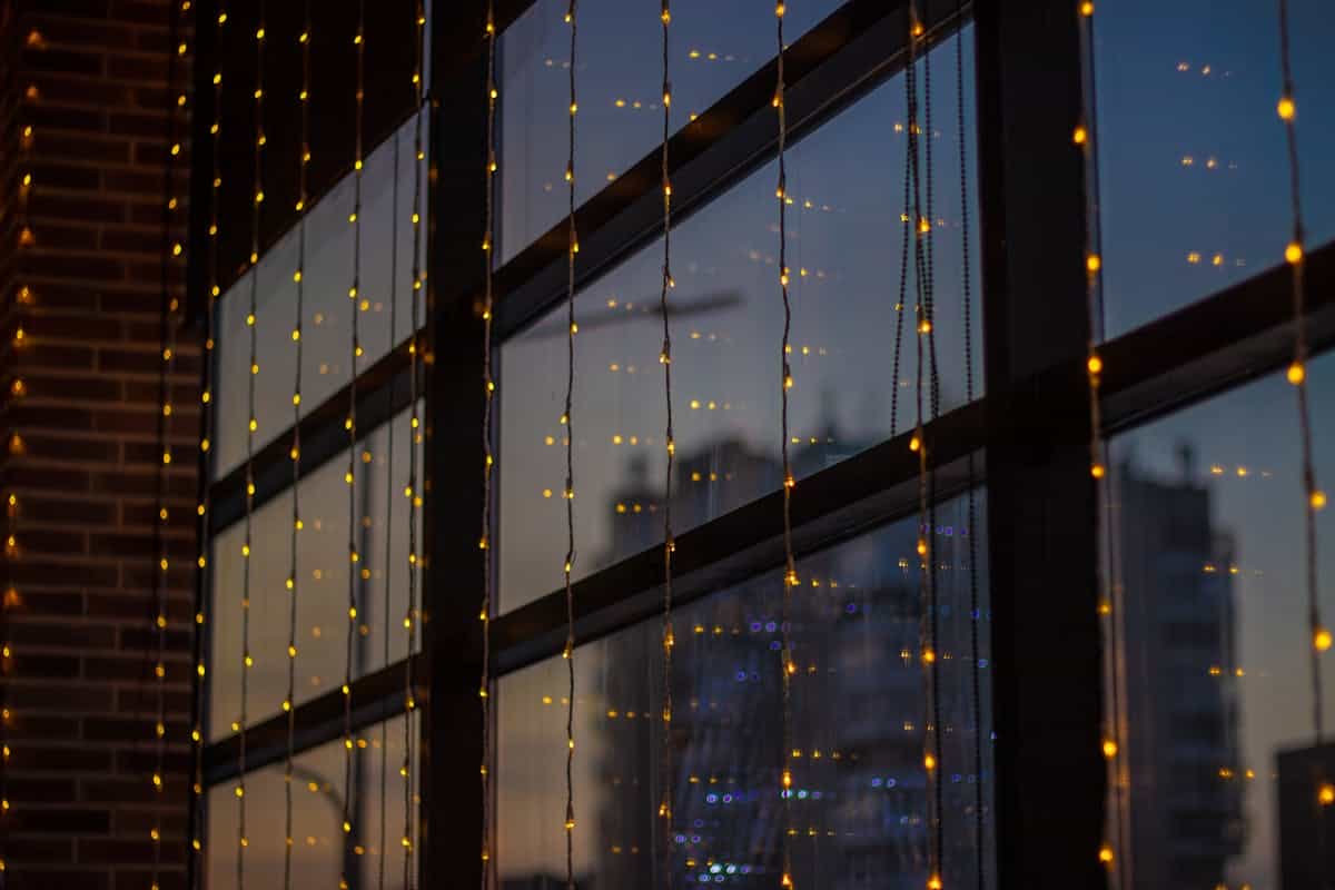 Evening window reflection with city lights merging inner and outer worlds metaphorically Twilight cityscape reflection through home window with fairy lights blending interior and exterior worlds