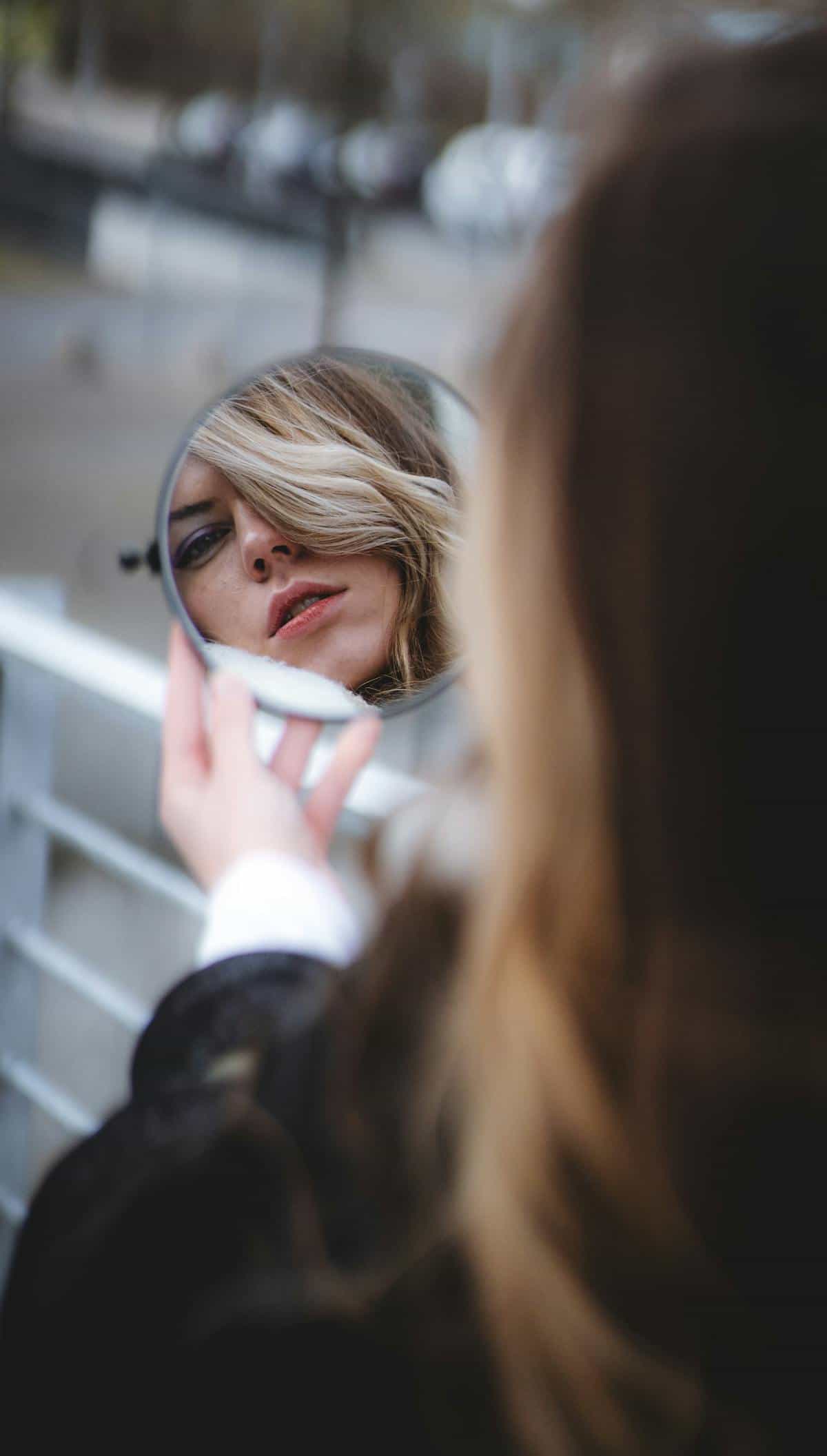 Woman holding a round mirror reflecting her face outdoors Blonde woman outdoors holding a small round mirror reflecting her face symbolising self-examination and identity in mirror dreams