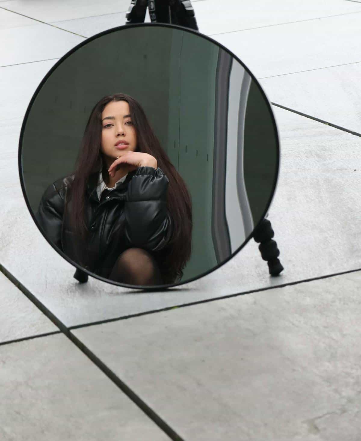 Urban sidewalk round mirror reflection portrait Young woman reflected in round mirror on urban sidewalk suggesting public identity and self-presentation themes