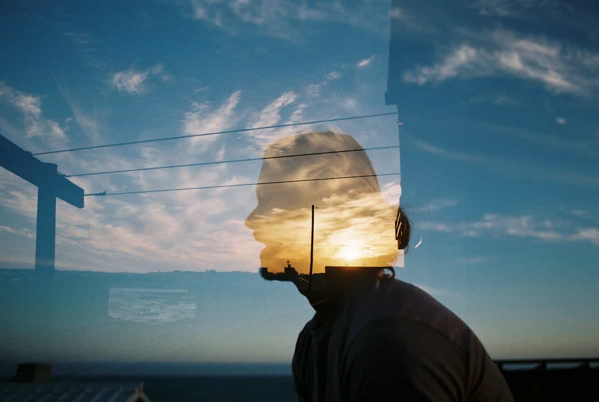 Artistic double exposure portrait with a silhouette merged with a landscape sky representing the dreamer examining past and future versions of self in a mirror dream