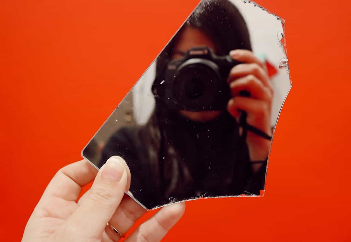 Creative self-portrait captured through a broken mirror against a vivid red background representing visual art's use of fragmented reflection and fractured identity