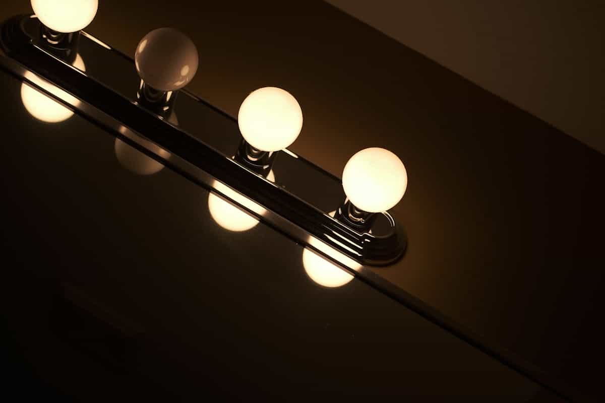 Vanity light fixture reflecting off a mirror illustrating the best vanity mirror lighting Contemporary vanity light fixture with glowing bulbs reflecting off a mirror, illustrating vanity mirror lighting
