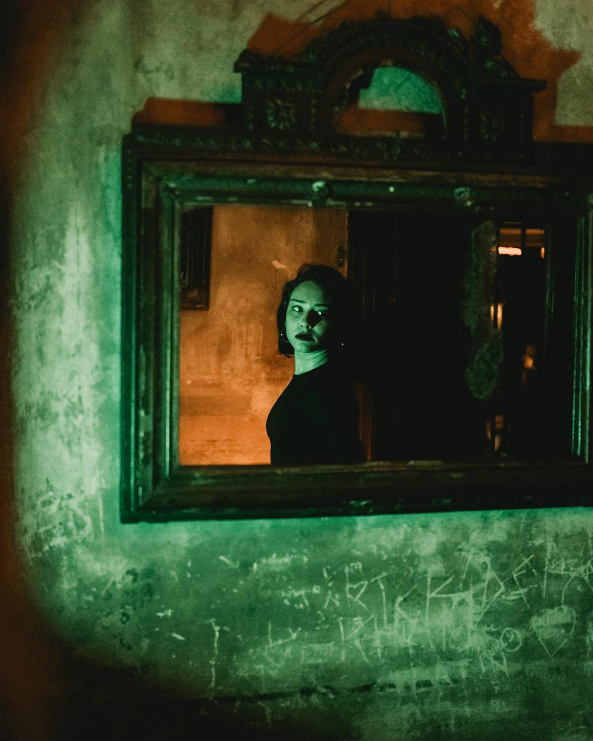 Ornate vintage mirror reflecting a solemn face under green ambient light hinting ceremonial mirror practice