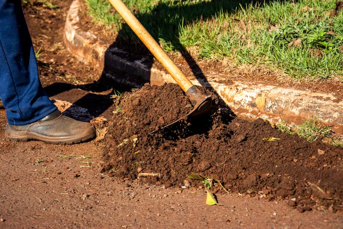 Hands carefully sweeping broken glass shards with a brush into a dustpan against a dark tile floor
