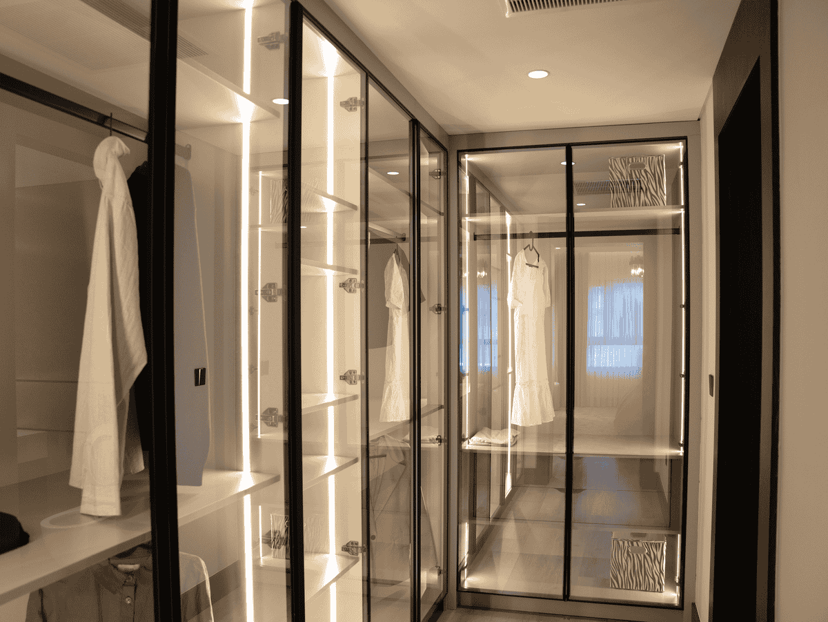 Walk-in wardrobe with glass doors and integrated LED lighting illuminating a mirrored wardrobe