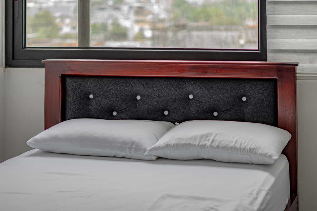 Bed with a solid wooden headboard against a wall illustrating the commanding position feng shui rule Modern bedroom with a wooden headboard and bed against a solid wall, illustrating the feng shui commanding position