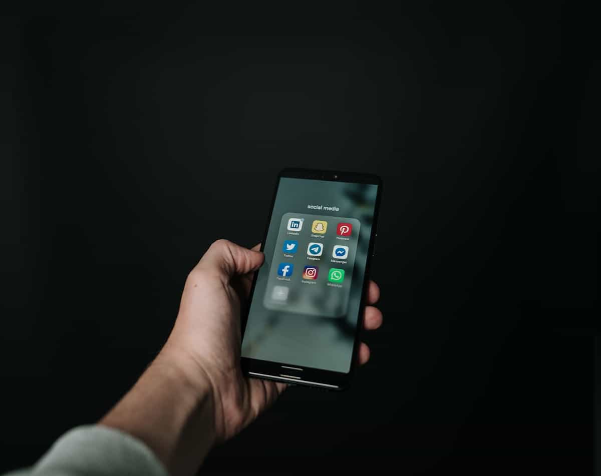 Hand holding smartphone showing glowing screen in dim setting suggesting late night social scrolling