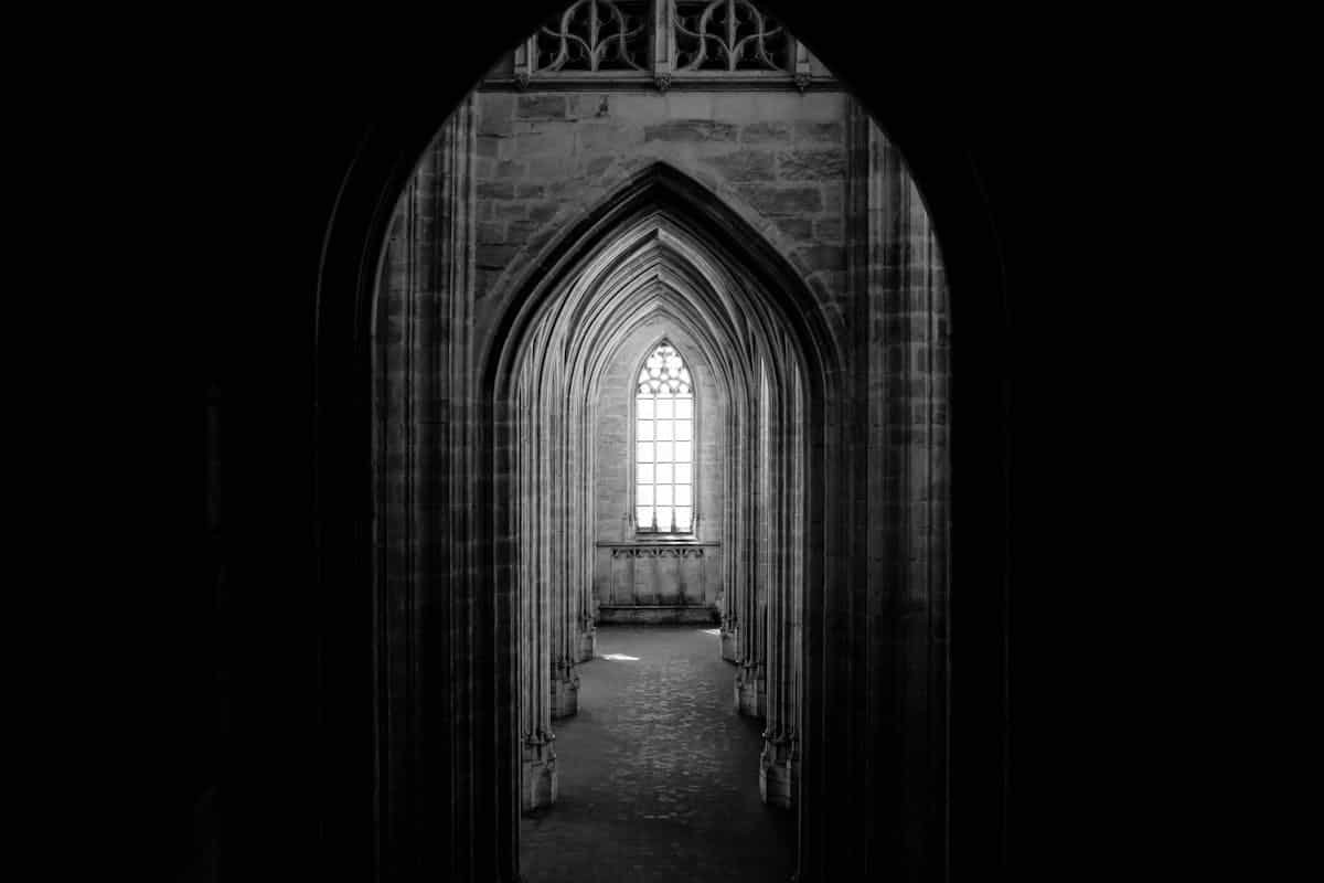 Monochrome interior of a vaulted historic corridor leading toward a distant window