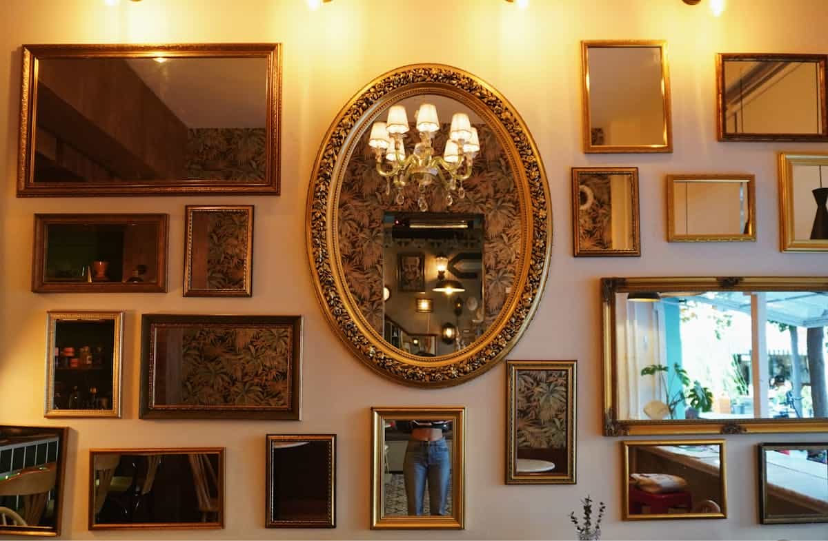 Wall of grouped framed mirrors illustrating how to group arched mirrors as a display Charming cafe wall with a variety of framed mirrors and a chandelier, illustrating grouped arched mirror decor