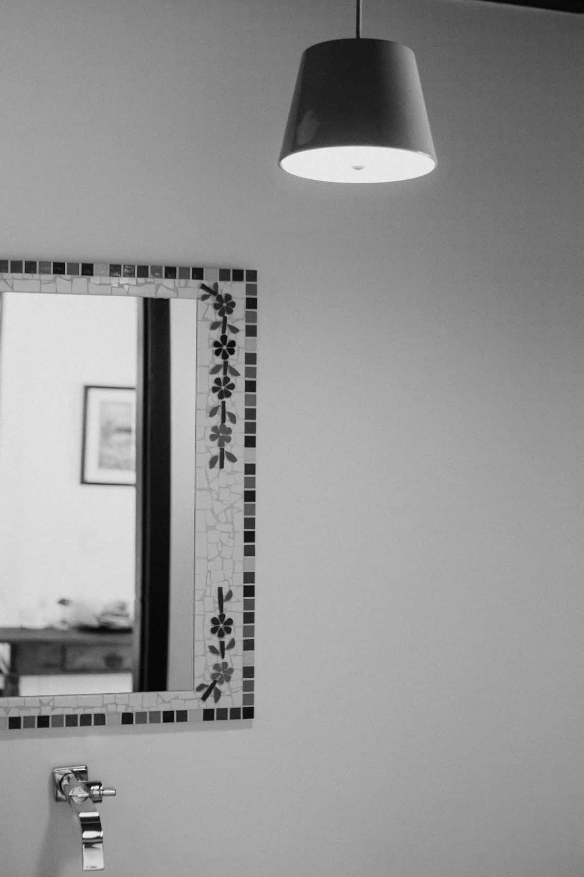 Minimalist black and white bathroom with decorative tiled mirror and natural light fixture illustrating the feng shui mirror facing window question and light redirection