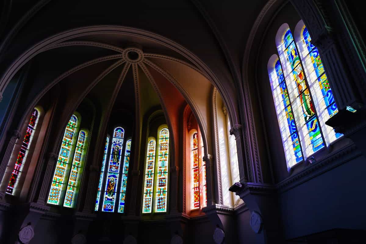 Vibrant stained glass windows in a gothic cathedral interior capturing colorful light representing the spiritual clarity that Scripture promises against the dim glass darkly of present understanding