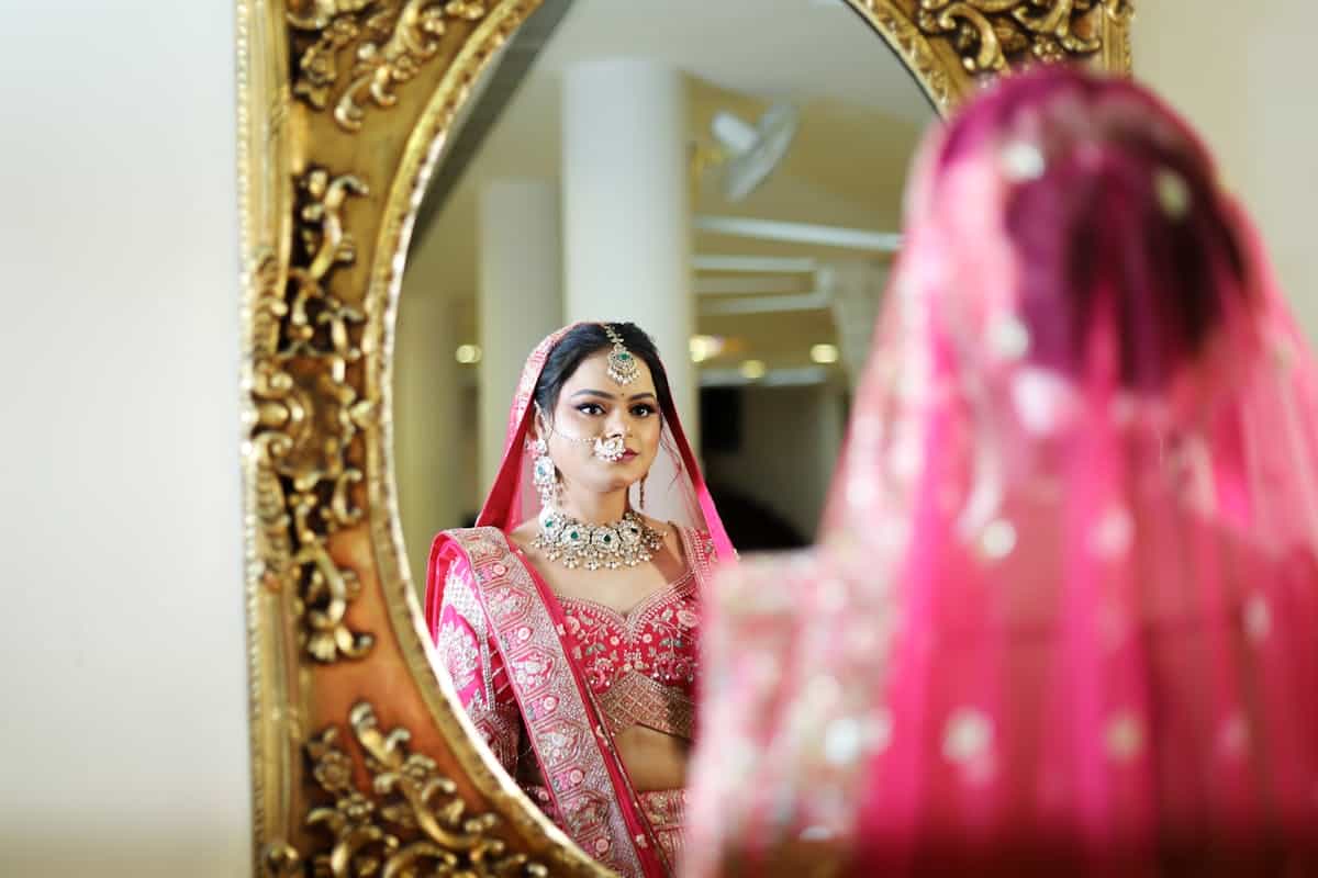 Beautiful bride in traditional Indian attire gazing into an ornate mirror, embodying the widespread superstitions around mirrors during weddings, pregnancy, and mourning