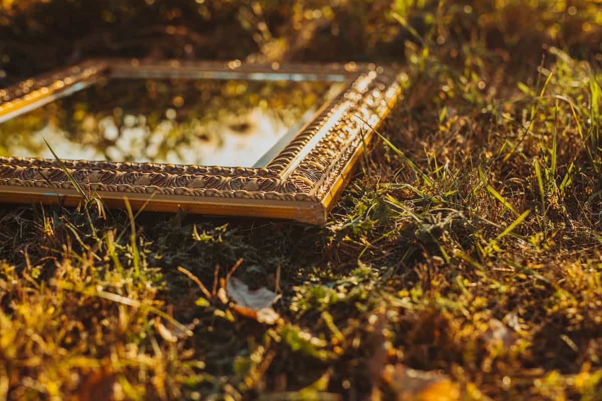 A vintage mirror reflecting golden sunlight on a grassy field at the golden hour, representing the less-known tradition of positive mirror superstitions and good-luck mirror beliefs