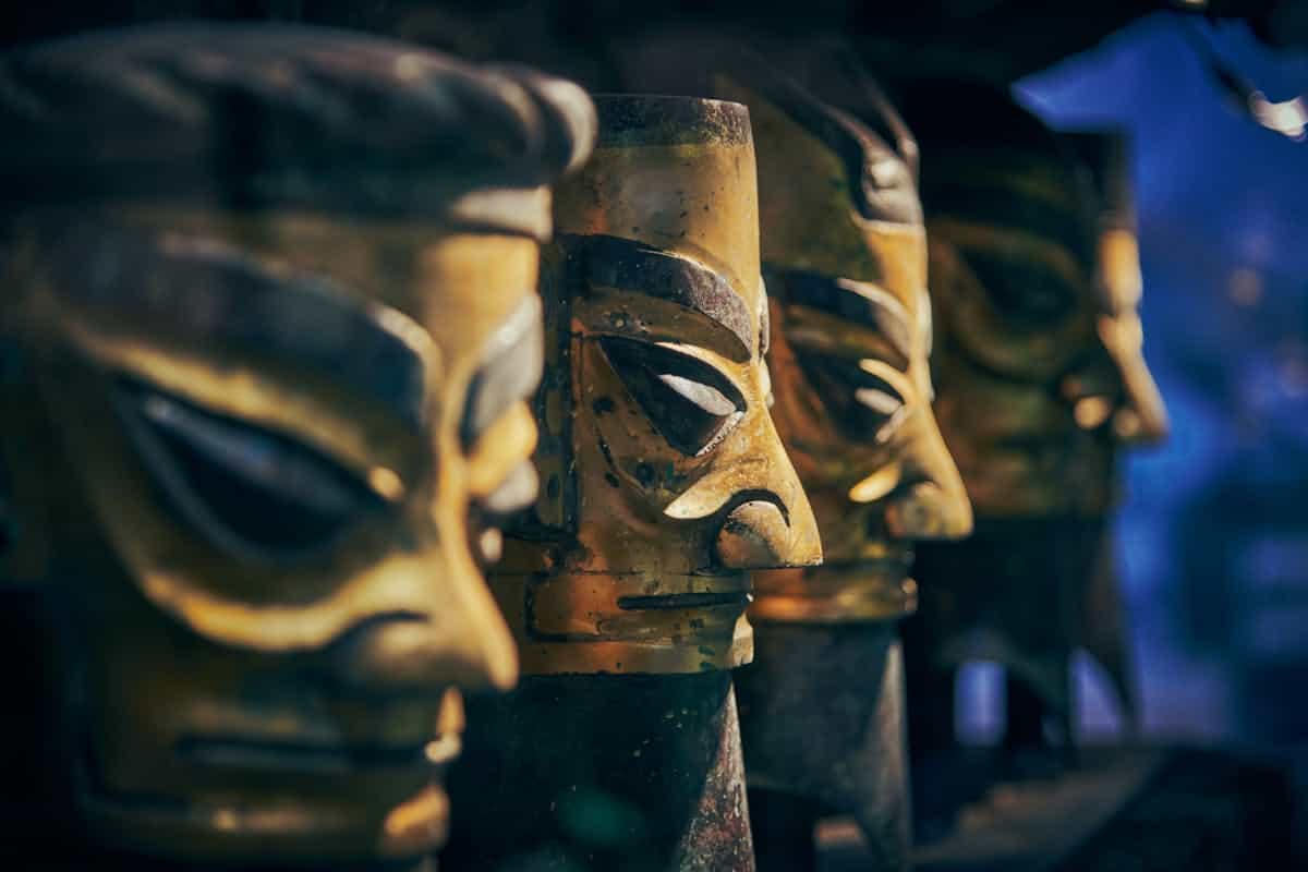 Dramatic golden mask statues in ceremonial lighting suggesting the visionary dimension of the magic mirror in ancient Egypt Intricately detailed golden mask statues in dramatic moody lighting evoking the trance states and ceremonial vision sought through Egyptian catoptromancy and magic mirror divination