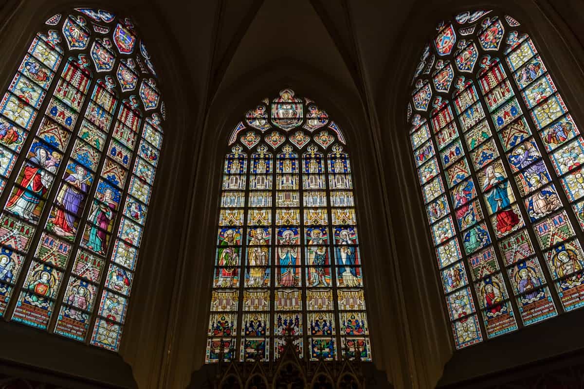 Intricate stained glass windows in a Gothic style church in Brussels representing the indirect beauty of seeing God through the glass darkly of human understanding