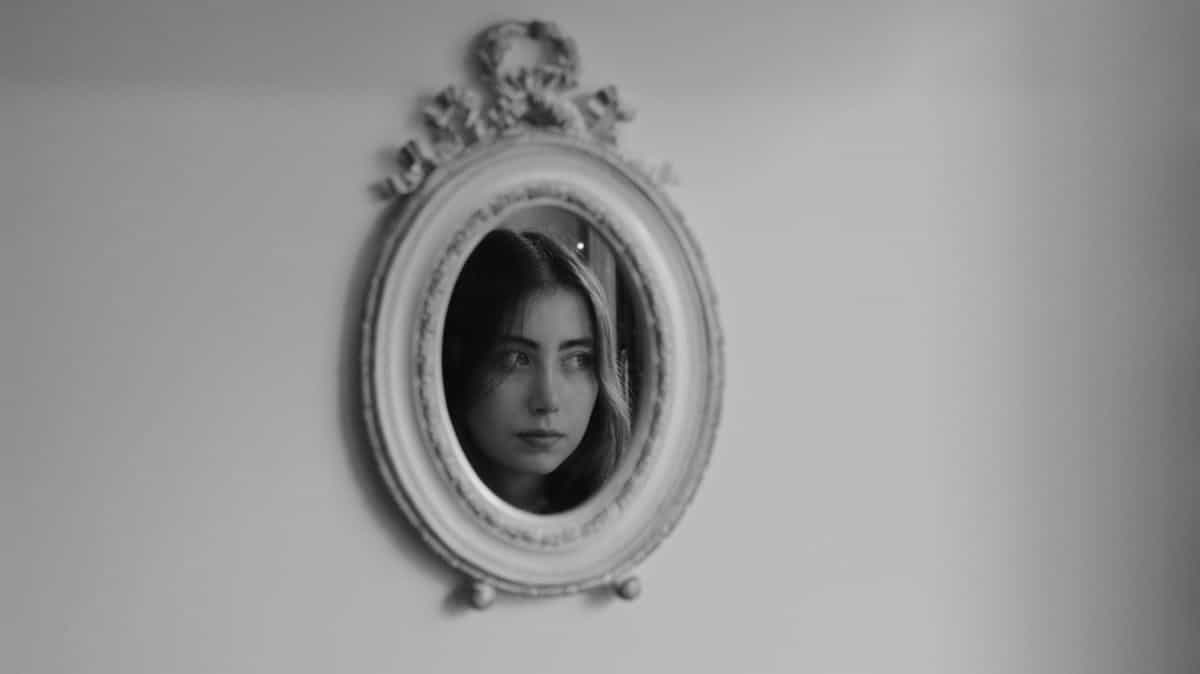 Artistic oval ornate mirror reflection portrait in black and white Black and white artistic reflection of a woman in an oval ornate mirror evoking soul double and identity symbolism