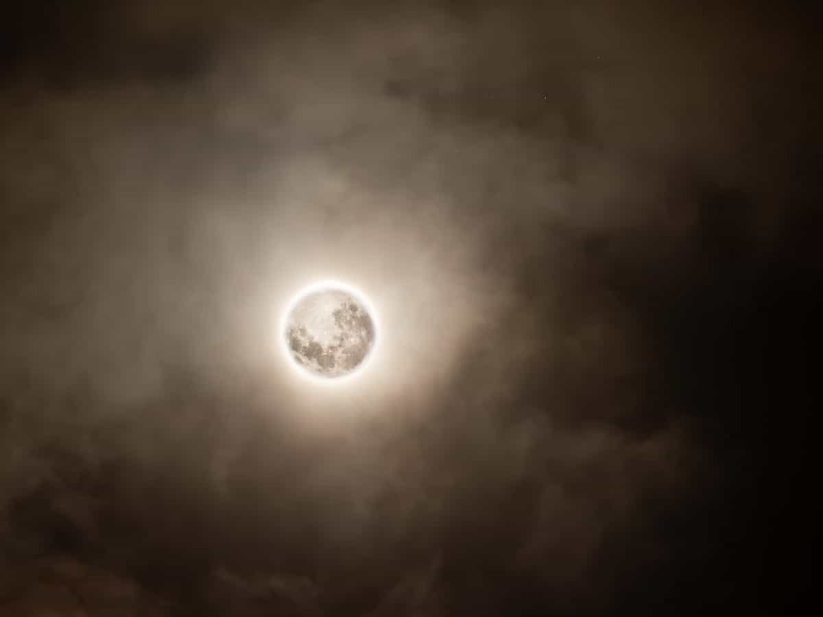 Full moon rising large and bright in a clear dark sky over a calm body of water with light reflecting on the surface