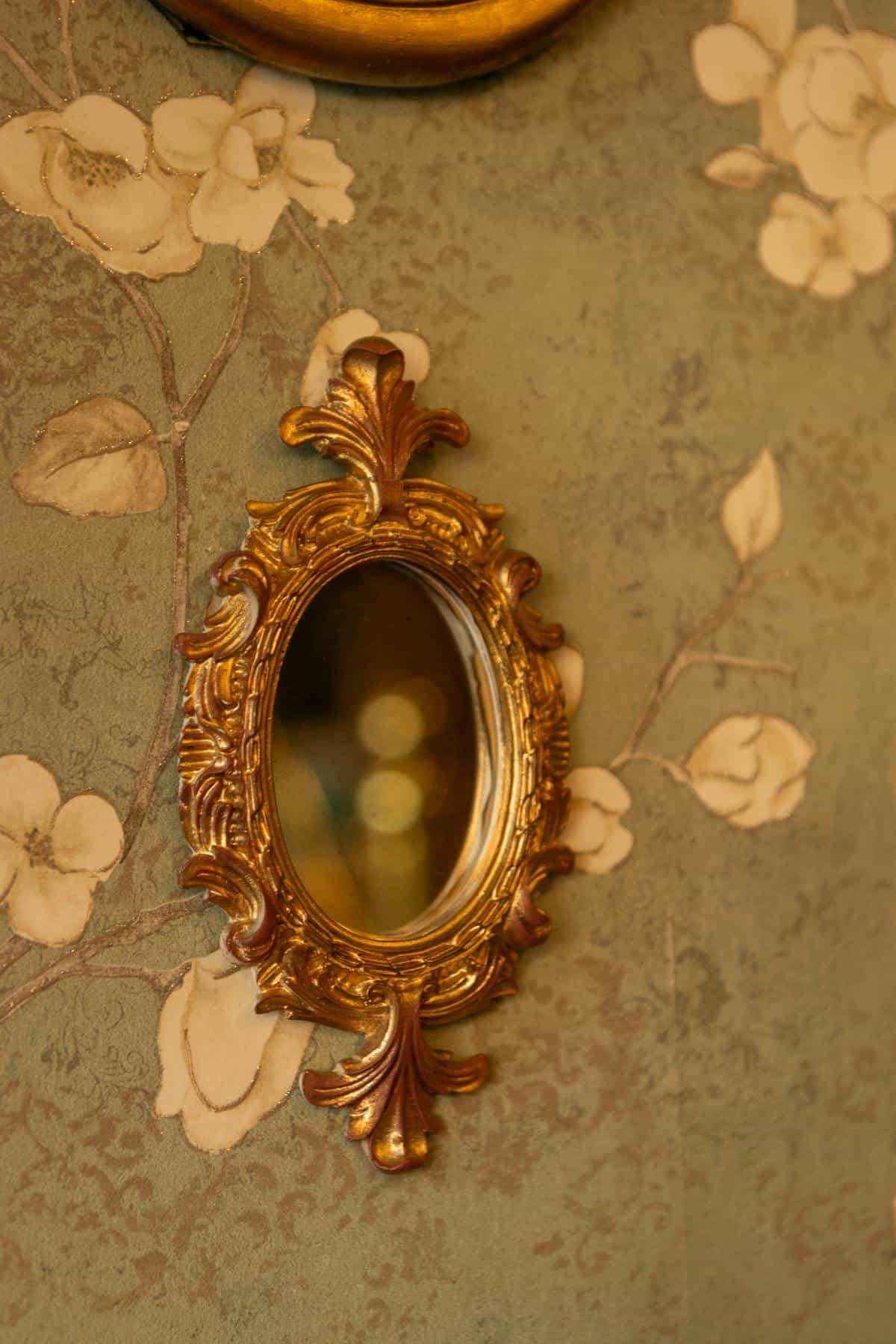 Ornate antique gold mirror on floral wallpaper in interior setting Antique ornate gold mirror on floral wallpaper evoking cultural history of mirrors beauty and superstition
