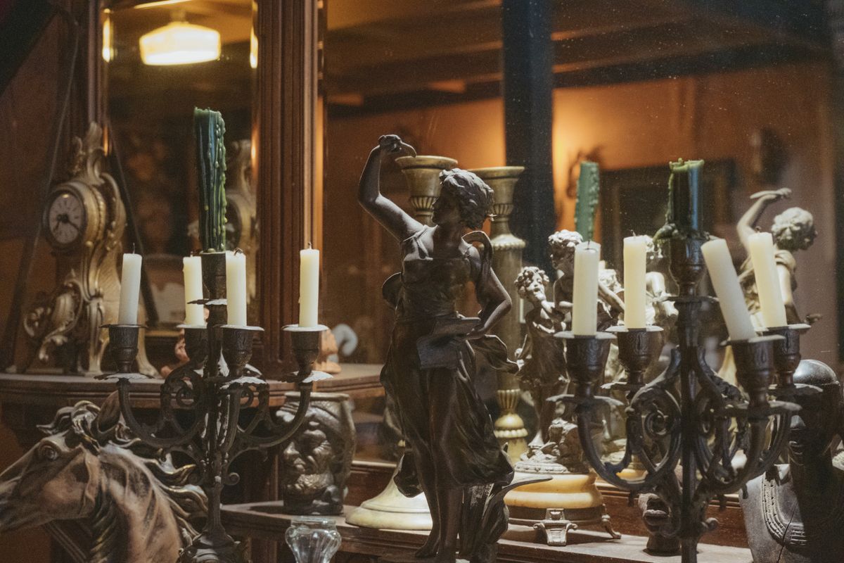 Antique statues and candle holders arranged in a dimly lit room evoking the atmosphere of ancient ritual and divination