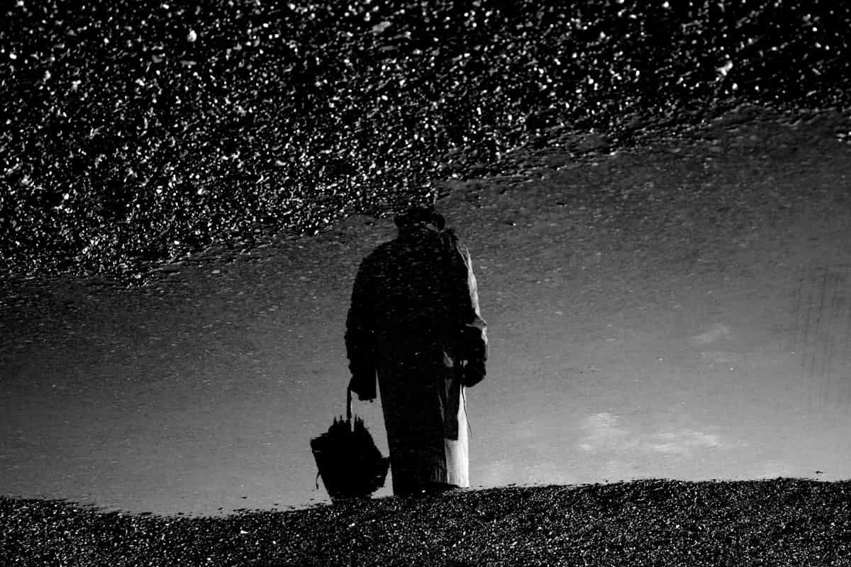 Silhouette of a person reflected in a rain puddle on a textured surface creating a dramatic and contemplative scene, representing the importance of staying grounded after black mirror sessions