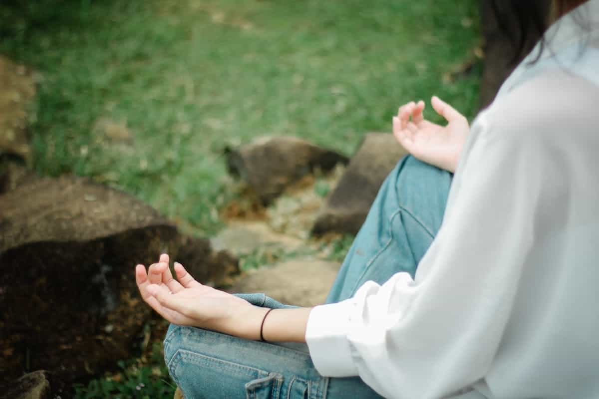 Person meditating outdoors in a calm natural setting with hands resting on knees