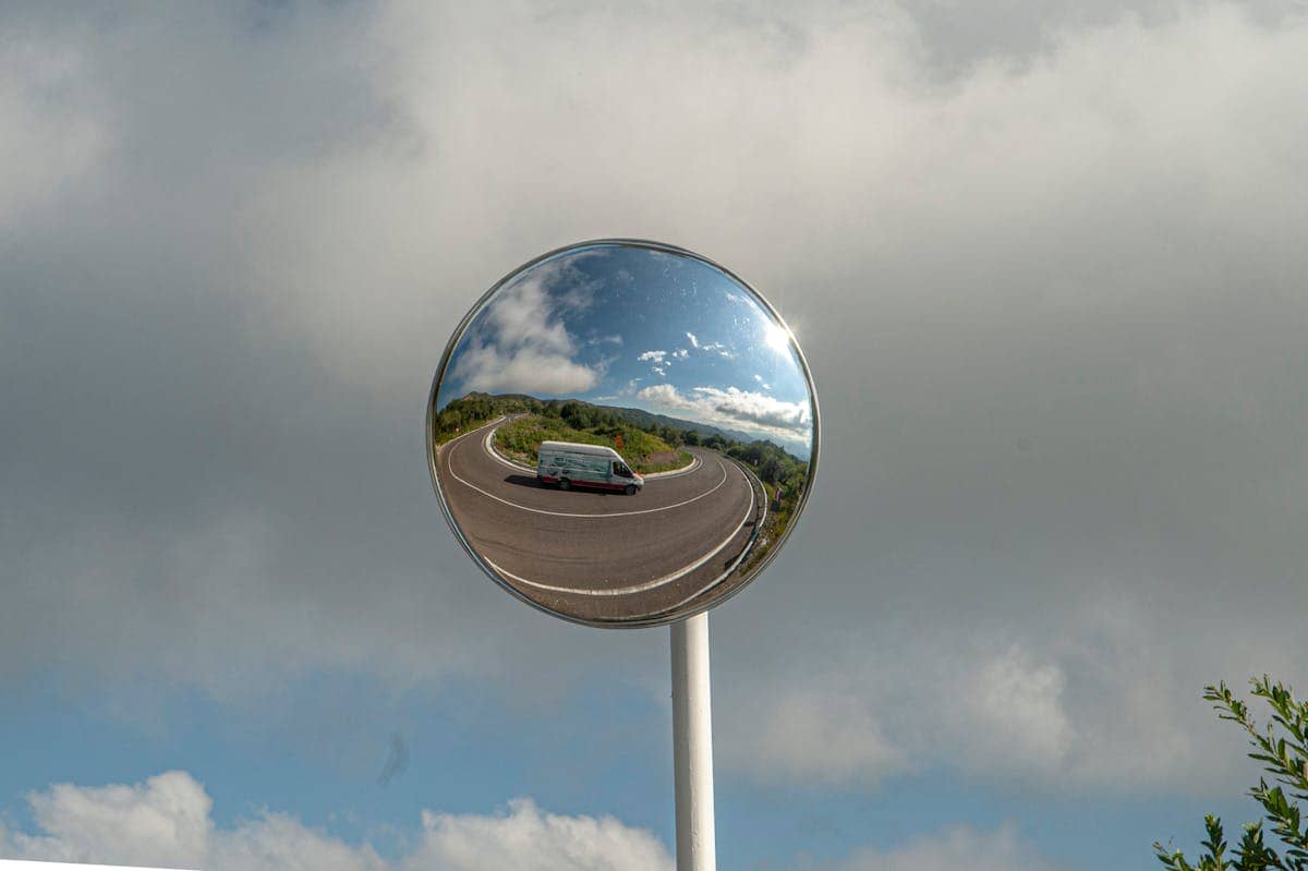 Curved convex traffic mirror reflecting a road and vehicle against a cloudy sky showing how everyday specular reflection has a precise quantum electrodynamic explanation in photon and electron interactions