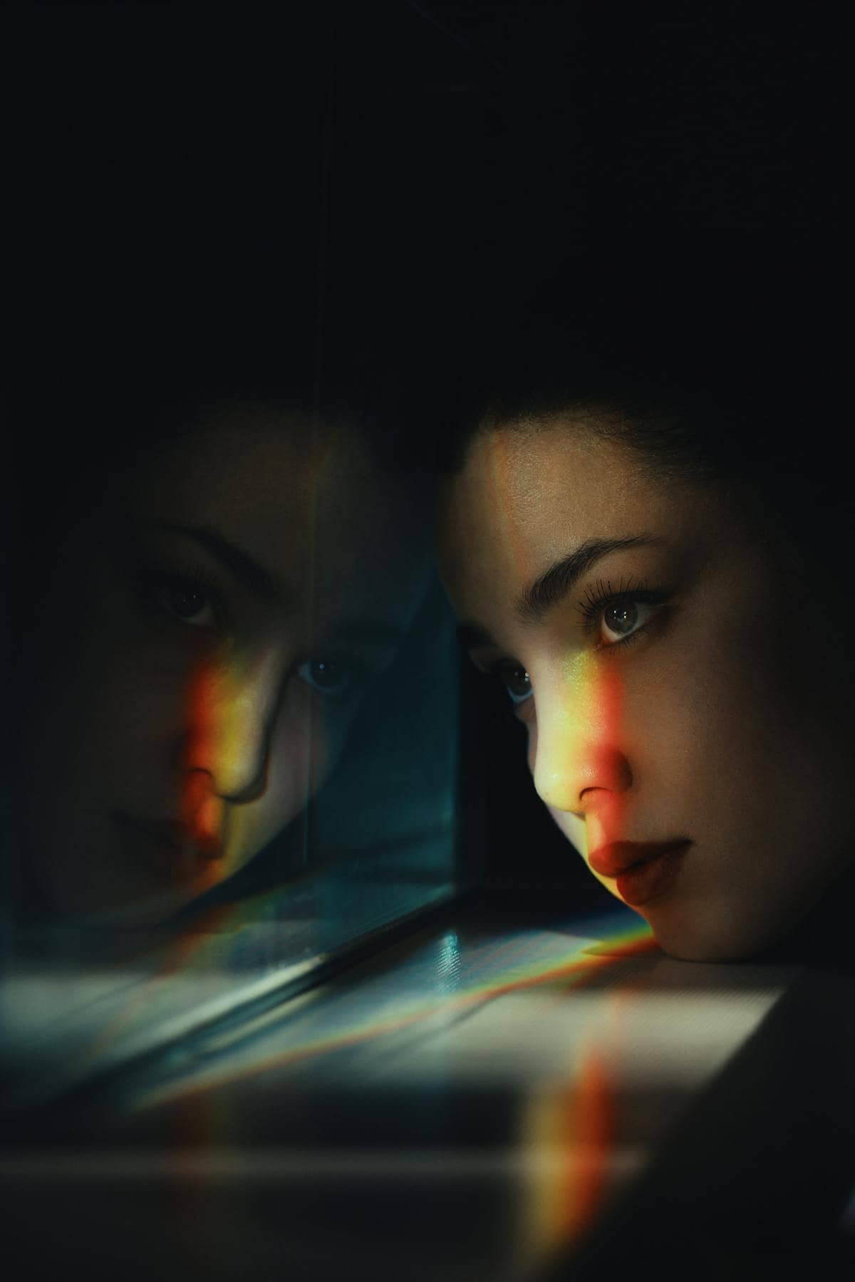 Portrait of woman studying reflection during dramatic directional lighting emphasizing facial planes and mirrored depth cues